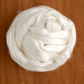 A ball of soft, white Cultivated Mulberry Silk Top is displayed on a wooden surface, showcasing its smooth and fluffy texture. This product from Europa Wools Ltd appears dense and neatly arranged in a circular shape.