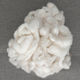 A collection of Silk Cocoons from Indian Silk Shop rests on a textured gray background. The cocoon fibers, resembling fluffy white cotton, appear soft and loosely gathered, highlighting their natural and unprocessed form.