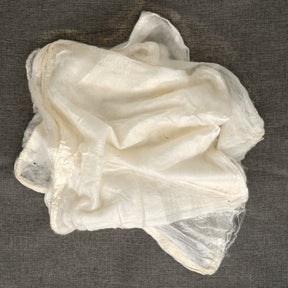 A crumpled, sheer piece of white cloth from the Silk Bombyx Hankies set by Europa Wools Ltd is displayed against a gray background. The delicate fabric, reminiscent of fine hankies, appears slightly translucent with soft folds and creases that reveal its exquisite continuous fibers.