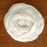 A coiled bundle of Europa Wools Ltd Rayon Top, a soft, white cellulose fiber sold by the ounce, rests on a wooden surface, resembling a fluffy swirl.