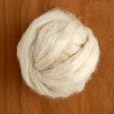 A close-up of a light beige ball of Europa Wools Ltd's Hemp Sliver Fiber, sold by the ounce, resting on a wooden surface. The fiber, in its soft and fluffy texture, intertwines into a neat, rounded shape.