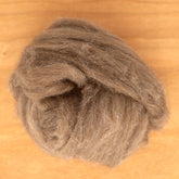 A ball of Europa Wools Ltd's Yak Down Fiber, a luxuriously soft brown wool roving blended with yak fiber, sits on a wooden surface.