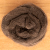 A close-up of a roll of luxuriously soft dark brown Yak Down Fiber from Europa Wools Ltd on a wooden surface. The fibers are neatly coiled, appearing soft and dense.