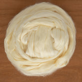 A close-up of a ball of cream-colored Soysilk® by Dashing Mouse, coiled in a circular shape on a wooden surface. This soft and slightly fluffy fiber, enhanced with renewable soy fiber, is perfect for spinning or felting while being eco-friendly.