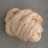 A close-up of a luxurious ball of beige yarn, combining the exquisite Camel Down & Tussah Silk Top from Dashing Mouse, resting on a textured gray fabric background. This silky yarn boasts a soft, fluffy appearance and is loosely wound.