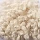 Close-up of a pile of Europa Wools Ltd Wool Nepps, showcasing their soft, fluffy, cream-colored fibers and unique yarn texture with a natural, textured appearance.