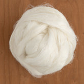 A close-up of a fluffy, white ball of Flax Roving from Europa Wools Ltd rests on a wooden surface. The fibrous texture and soft appearance suggest it is suitable for wet spinning, making it ideal for crafting or knitting intricate designs.