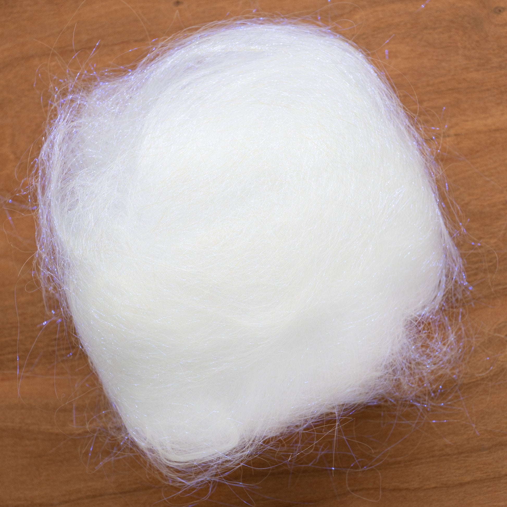 A product from Foxglove Fiberarts Supply, the Clearance! Crystal Mylar Fiber is a soft and fluffy bundle of white synthetic fiber woven with light-catching metallic mylar fibers. It rests atop a wooden surface, resembling a small cloud.