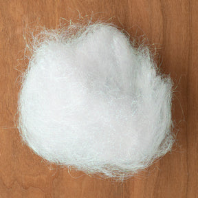 A tuft of Crystal Mylar Fiber from Foxglove Fiberarts Supply, reminiscent of a fluffy white cloud and featuring shimmering highlights, sits on a wooden surface.