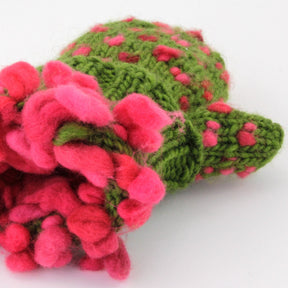 The Snuggly Stuffed Mittens from Halcyon Yarn feature a plush, knitted cactus with a green body and pink spots, adorned with vibrant pink flowers at the top. Crafted entirely from yarn, these elements provide a soft, fuzzy texture that resembles wonderfully warm fleece. The plush toy lies on a plain white background.