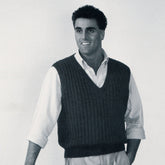 A smiling man with curly dark hair is wearing a tailored Moss Rib Vest from Bryson Distributing, Inc. over a white button-up shirt. He is standing with his left hand in his pocket and looking slightly to his right. The image is black and white.