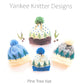 Four knitted "Pine Tree Hats" from Yankee Knitter Designs are displayed against a white background. These hats feature snowy tree patterns and pom-poms on top, and come in various color combinations. Text above the hats reads "Yankee Knitter Designs" and below, "Pine Tree Hat - Your perfect Vacationland keepsake hat.