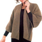 A person wearing the Basic Garter Stitch Kimono by Plymouth Yarn Co, a textured brown knitted cardigan with wide sleeves and an open front, over a black outfit. The person is adjusting the collar with one hand while the other hand rests by their side. The background is plain white.