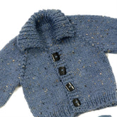 The Top Down Baby Jacket by Plymouth Yarn Co is a knitted blue sweater with a high, ribbed collar and four black square buttons down the front. It features an easy-to-knit design with a speckled pattern incorporating tiny white threads throughout the fabric.