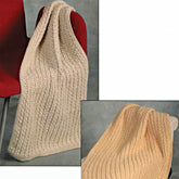 A luxurious Plymouth Yarn Co knitted cream [Lap Throw Pattern](https://example.com) is draped over a red chair, making it perfect for movie night. The close-up insert reveals the detailed intricacy of the patterned lap throw.