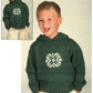 A young child smiles while wearing a dark green Child's Snowflake Hoodie by Plymouth Yarn Co., featuring a white geometric pattern on the chest. The child, with short blonde hair, stands with both hands in the pockets of their beige cargo pants. An inset of the same child in the hoodie is also shown.