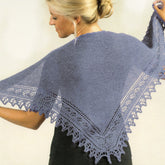 A person with blonde hair holds up a Shawlette Pattern from Plymouth Yarn Co, its intricate lace edging forming a triangular shape. The shawl drapes gracefully over the person's back as they face sideways, wearing a black top—perfect for a spring or summer look.