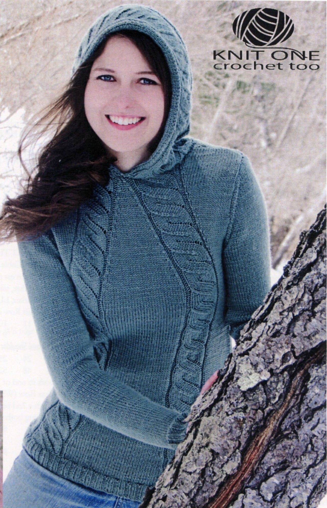 A woman stands outdoors in a snowy forest, smiling and wearing the Knit One, Crochet Too Faux Cable Hoodie in teal. She is leaning against a tree trunk. The text "Knit One, Crochet Too" is displayed in the top right corner.