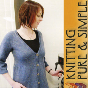 A person with short, brown hair is wearing a light blue Neck Down Swing Cardigan from Bryson Distributing, Inc., with buttons and a black top underneath. They are standing near a white wall next to a vertical banner that says "KNITTING PURE & SIMPLE." They appear to be adjusting a knitting machine ideal for creating all-season wear.