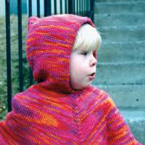 A little one with blonde hair stands outside near steps and a metal railing, wearing the fashionable Children's Hooded Poncho by Bryson Distributing, Inc., which features a pink and orange knit design with small, pointed ear-like protrusions. The child looks to the left, seemingly focused on something.