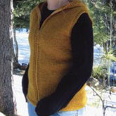 A person is wearing the Bryson Distributing, Inc.'s Bulky Hooded Vest for Women in a mustard color over a long-sleeved black shirt. They are standing outdoors near a tree with snow visible on the ground and additional trees in the background. The vest, crafted from bulky yarn, looks cozy and warm against the chilly backdrop.