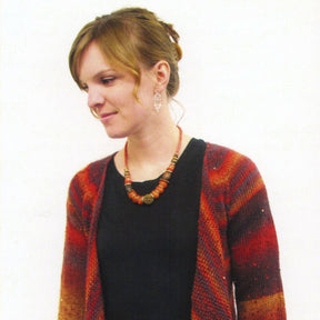 A woman with light brown hair styled in a loose updo is looking down and smiling slightly. She wears a black top under the Top Down Drape Front Cardi by Bryson Distributing, Inc., made of multi-colored yarn in shades of red and orange, accompanied by a beaded necklace and dangling earrings, set against a plain white background.