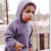 A toddler wearing a Bryson Distributing, Inc. Neck Down Hooded Tunic stands outside on a wooden deck, looking intently at something off-camera. The background features a blurry view of a fence, trees, and a car.