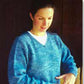 A person with long dark hair is wearing a light-weight blue Neck Down Pullover Tunic by Bryson Distributing, Inc. over a white top. They are looking down and extending their right arm, appearing to adjust or examine something with their left hand. The background is dark, and they are partially lit from the front.