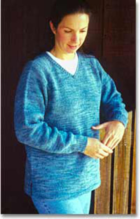 A person wearing the Neck Down Pullover Tunic from Bryson Distributing, Inc. and light blue jeans stands against a wooden background. They are looking down at their hands, which are positioned in front of their body. The person appears calm and thoughtful.