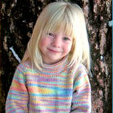 A young child with blonde hair stands in front of a tree trunk, smiling slightly. The child is wearing the colorful striped Child's Neck Down Pullover by Bryson Distributing, Inc., featuring a mix of pastel hues including pink, blue, yellow, and green. The background is shaded by the tree's textured bark.