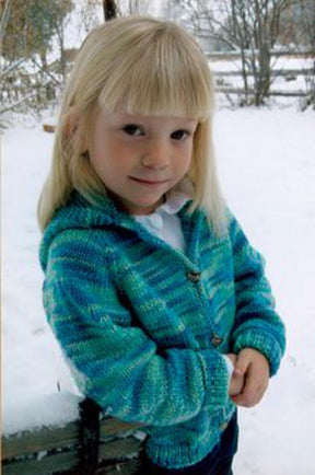 A young girl with blonde hair is smiling slightly in a snowy outdoor setting, wearing a blue and green Children's Neck Down Cardigan from Bryson Distributing, Inc. She stands with her hands clasped in front of her, and leafless trees are visible in the background.