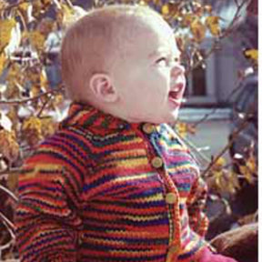 A light-skinned baby with short hair is smiling and looking to the right. The infant is wearing the Baby Neck Down Cardigan from Bryson Distributing, Inc., a colorful, striped, knitted sweater adorned with wooden buttons. They are outdoors amidst a backdrop of yellow and gold autumn leaves, showcasing some creative touches in their knit cardigan.