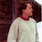 A man stands outdoors, wearing a Bryson Distributing, Inc. Neck Down Pullover over a red shirt, looking to the right. The background features a wooden building with icicles hanging from the roof and snow on the ground.