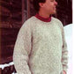 A man stands in the snow, facing to the right and smiling. He is wearing a thick, light gray Neck Down Pullover by Bryson Distributing, Inc., over a red high-neck shirt. In the background is a wooden structure with icicles hanging from the roof.