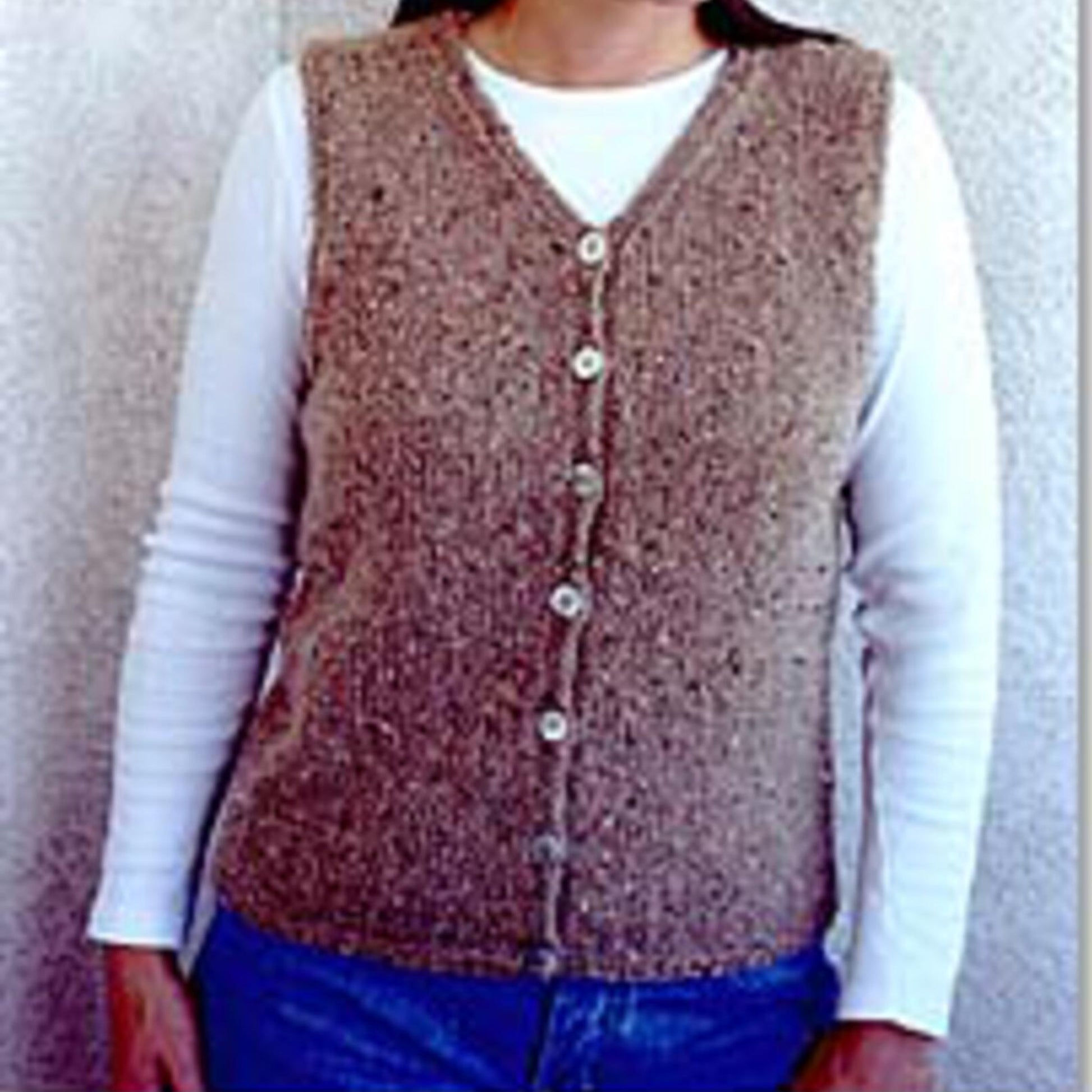 A person is wearing a white long-sleeve shirt paired with a simple brown V-Neck Vest from Bryson Distributing, Inc., standing against a plain textured wall, with only their upper body visible.