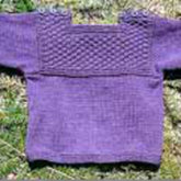 A delightful Fisherman T-Shirt Pullover Sweater for Baby Pattern by Bryson Distributing, Inc., featuring a textured square design on the chest, is beautifully displayed flat on green grass.