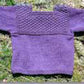 The Bryson Distributing, Inc. Fisherman T-Shirt Pullover Sweater for Baby Pattern is a delightful knitted infant sweater in purple, showcasing a textured chest design and shoulder button details. Laid flat on a grassy background, it exudes an adorable fisherman style.