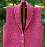 The Village Vest by Bryson Distributing, Inc., a sleeveless pink knitted piece with four white buttons down the front, is displayed on a wooden hanger. This shawl-collared cardigan offers extra warmth and a tailored look, set against a blurred green outdoor background.