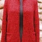 The Montreal Jacket by Bryson Distributing, Inc. is showcased on a black mannequin, ideal for both a night out and office wear. This red knitted cardigan features a straightforward, open front design without buttons and includes two front pockets. The background consists of a stone wall.