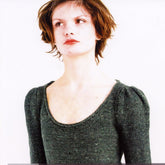 A person with short, tousled hair wears the Heathers Pullover by Knitting Fever / Euro Yarns, featuring a delicate horseshoe lace pattern and a green scoop neck design. They have a pensive expression and are looking upward against a plain white background.