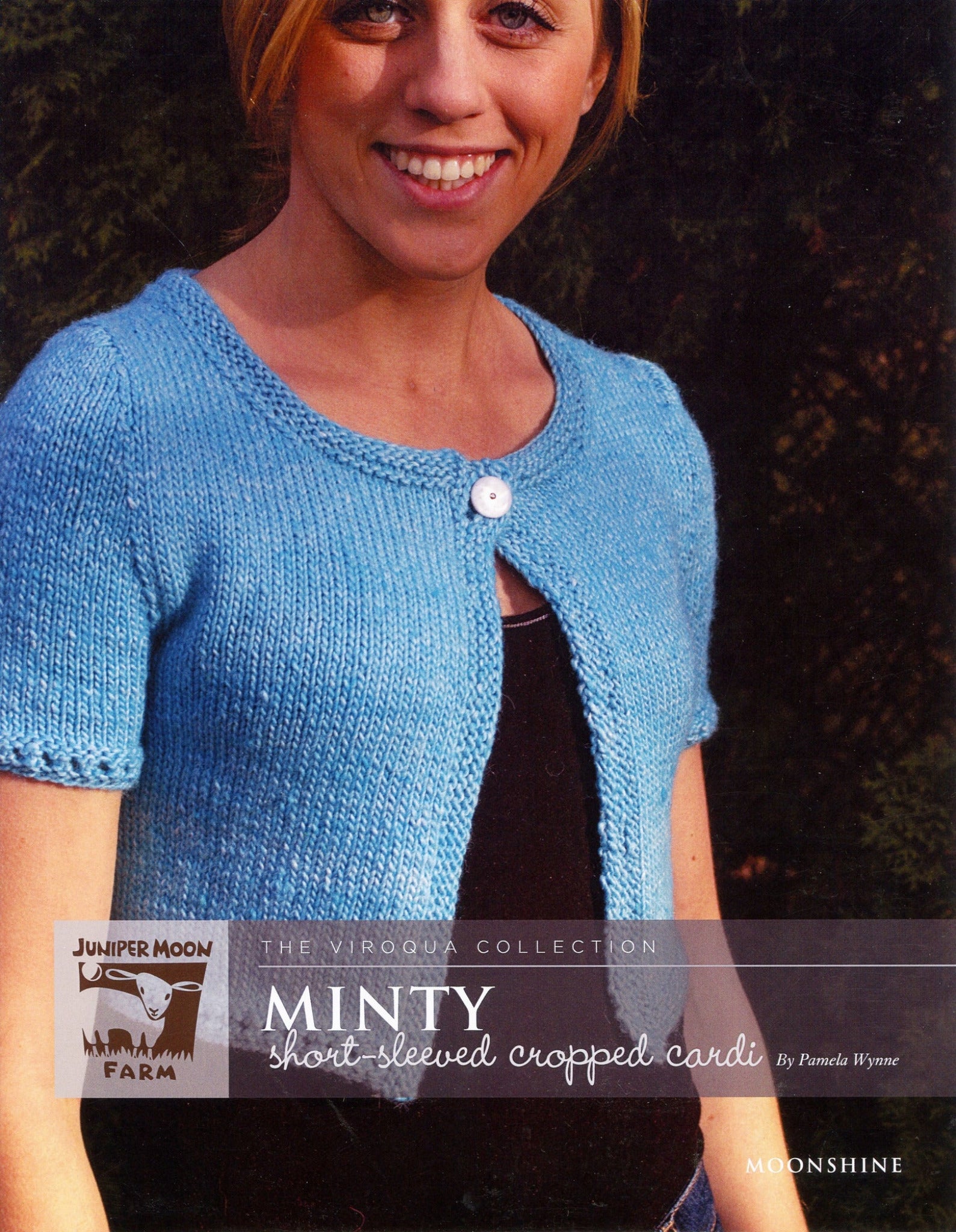 A cover photo of a knitting pattern called "Minty Short-Sleeved Cropped Cardi" from Knitting Fever / Euro Yarns' Viroqua Collection. The image showcases a woman wearing a swingy short-sleeved cropped blue cardigan with a white button. Designed by Pamela Wynne, this Moonshine Pattern from Juniper Moon Farm makes for an excellent layering piece for summer dresses.