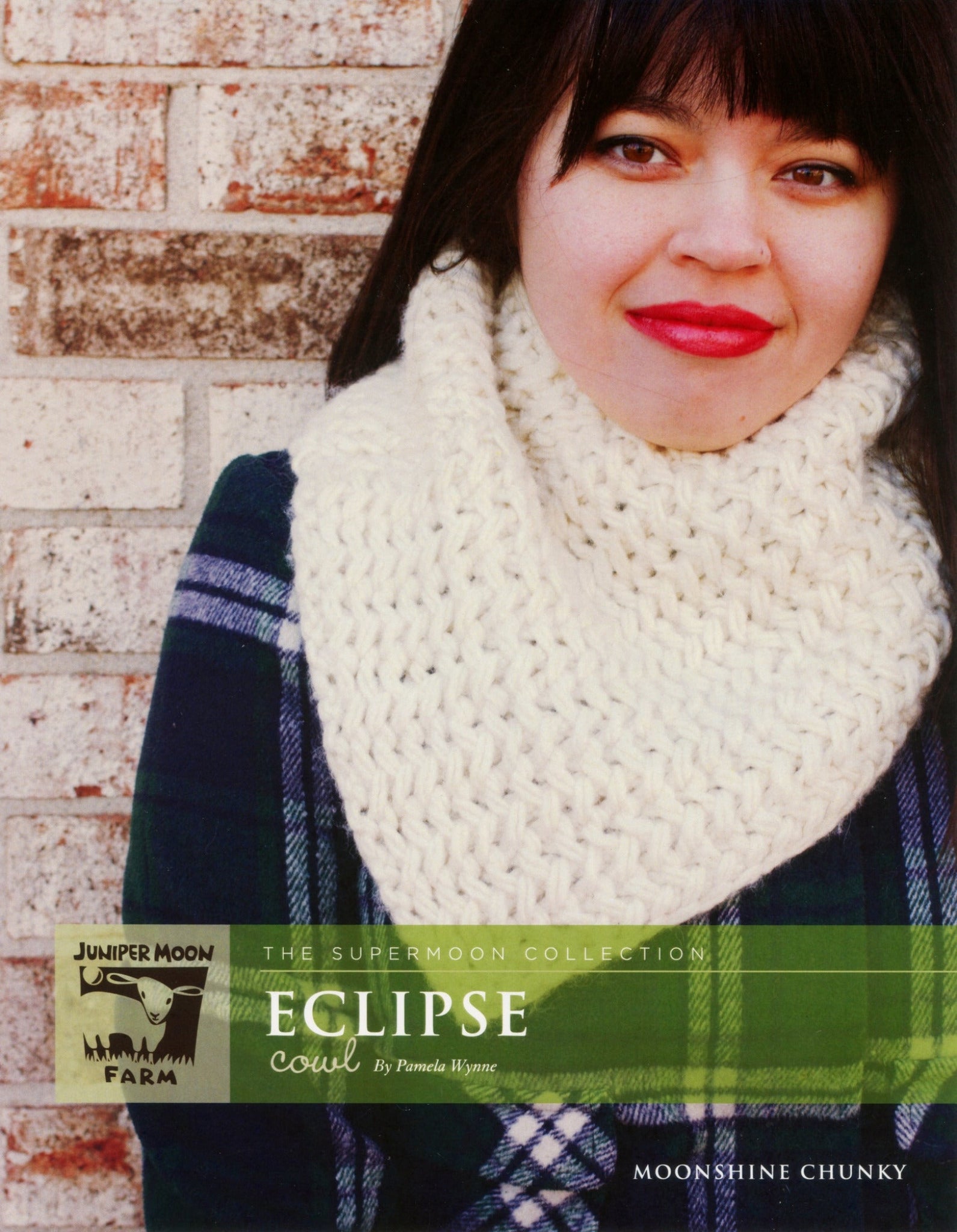 A woman with dark hair and red lipstick wears a white chunky knit cowl over a blue and green plaid shirt. The background is a brick wall. Text on the image reads: "The Supermoon Collection: Eclipse Cowl from Knitting Fever / Euro Yarns" and "Moonshine Chunky Bulky Yarn." The Juniper Moon Farm logo is also visible.