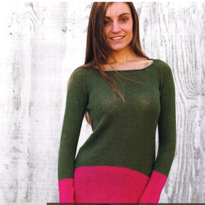 A person with long brown hair, wearing the Echo Tunic Pattern from Knitting Fever / Euro Yarns, featuring a green and pink color-blocked design, stands smiling against a textured white background.