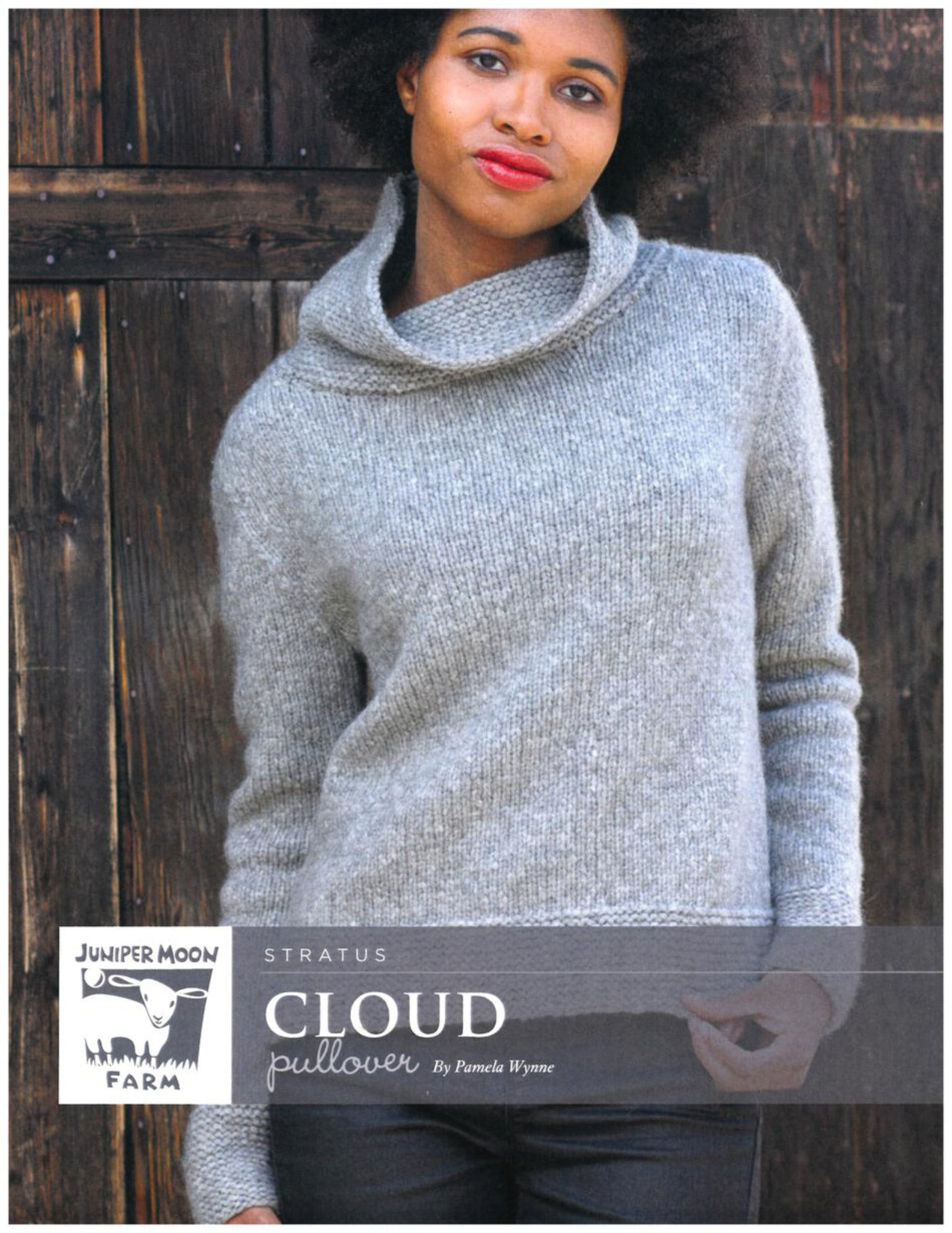 A person with medium-length curly hair is wearing a grey, knitted Stratus Cloud Pullover from Knitting Fever / Euro Yarns, made from Aran weight yarn and featuring a loose, wide collar. The individual stands in front of a rustic wooden background, with hands in the pockets of their jeans. The text on the image reads "Cloud Pullover by Pamela Wynne.