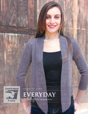 A person with long brown hair is standing in front of a wooden background, wearing a gray alpaca sweater over a black top. The text on the image reads, "Knitting Fever / Euro Yarns Herriot Fine Everyday Cardigan by Pamela Wynne.