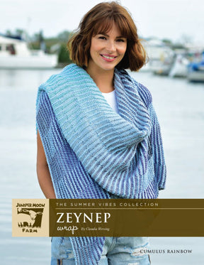 A woman stands near a harbor wearing a blue and purple knitted Cumulus Rainbow Zeynep Wrap from the Summer Vibes Collection by Claudia Wersing. Text on the image includes "Knitting Fever / Euro Yarns." The background features boats and a partly cloudy sky.