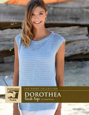 A woman is smiling and wearing a light blue, knitted tank top. She has long, light brown hair and is standing outdoors in front of a wooden background. Text on the image reads "Knitting Fever / Euro Yarns, Cumulus Dorothea Tank Top by Claudia Wersing." This versatile piece makes a perfect summer tank top or swimsuit cover up.