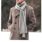 A man wearing a camel-colored coat and a gray scarf stands against a blurred, natural background. The text below the image describes the Roscoe Scarf by Blue Sky Fibers, highlighting its versatile reversible rib design for men and women, made with Eco-Cashmere for warmth.