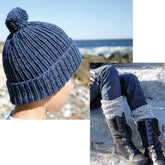 A person is wearing the Candide Ragg Socks & Cap #38 from Halcyon Yarn, a blue knit hat with a pompom, standing outdoors near the sea. Another image shows the same person sitting on rocks, wearing knitted leg warmers made from wool yarn and black lace-up boots over jeans, with the sea visible in the background.