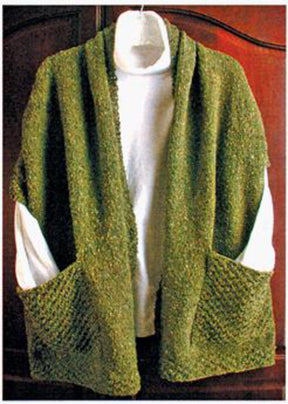 A green, textured knit cardigan, known as the Reader's Wrap by Lisa's Knits, hangs gracefully draped over a white hanger. This cozy piece, ideal for those chilly moments, is showcased against a wooden background and seems to be layered over a white shirt. Two large front pockets add both style and functionality to this elegant cardigan.